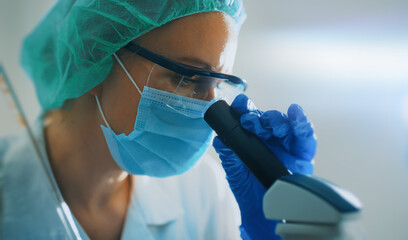 Scientist in medical mask working with microscope in lab.