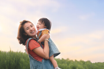 Happy Asian mother plays with daughter and holding girl in hands at park with nice sky, Baby smile and laughing,  Family concept.