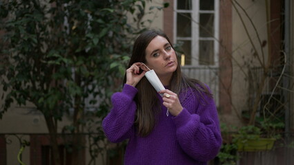 Young woman putting covid-19 surgical face mask looking at camera