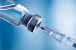 Glass vial and syringe with injection over blue background. Vaccination or beauty therapy concept.