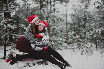 Two young teenage hipster girl friends together.Close up fashion portrait of two sisters hugs and having fun winter time,wearing red santa hats and sweater,best friends couple outdoors, snowy weather