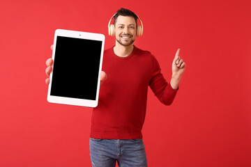Man with big tablet computer and headphones pointing at something on red background