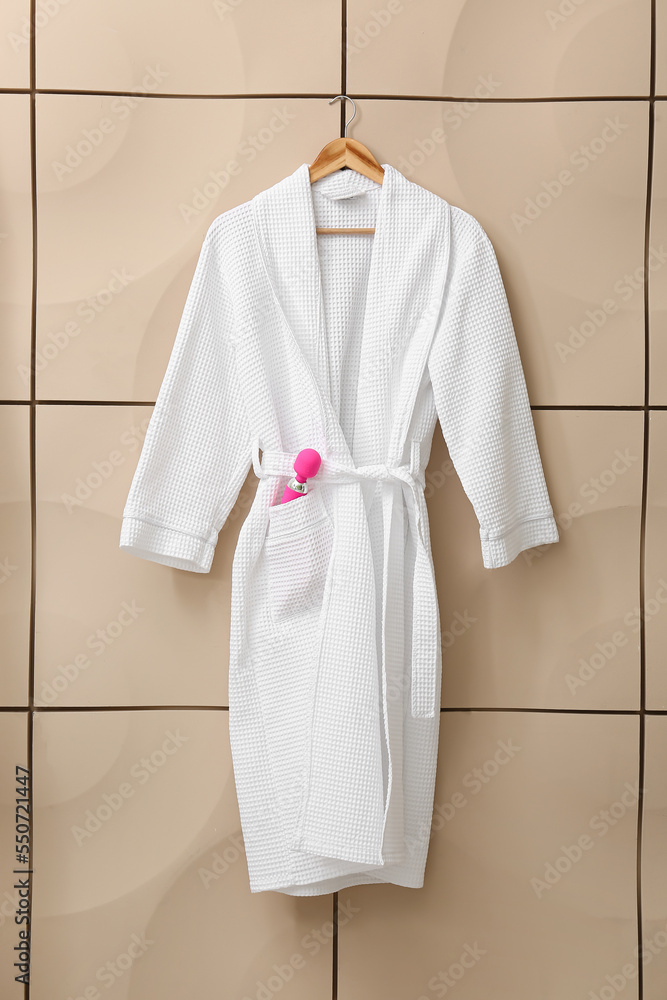 Bathrobe with pink vibrator hanging on beige wall
