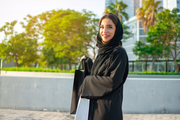 Wall Mural - Young muslim woman enjoying shopping time in the city of Abu Dhabi. Beautiful Arabic woman with shopping bags on the street.