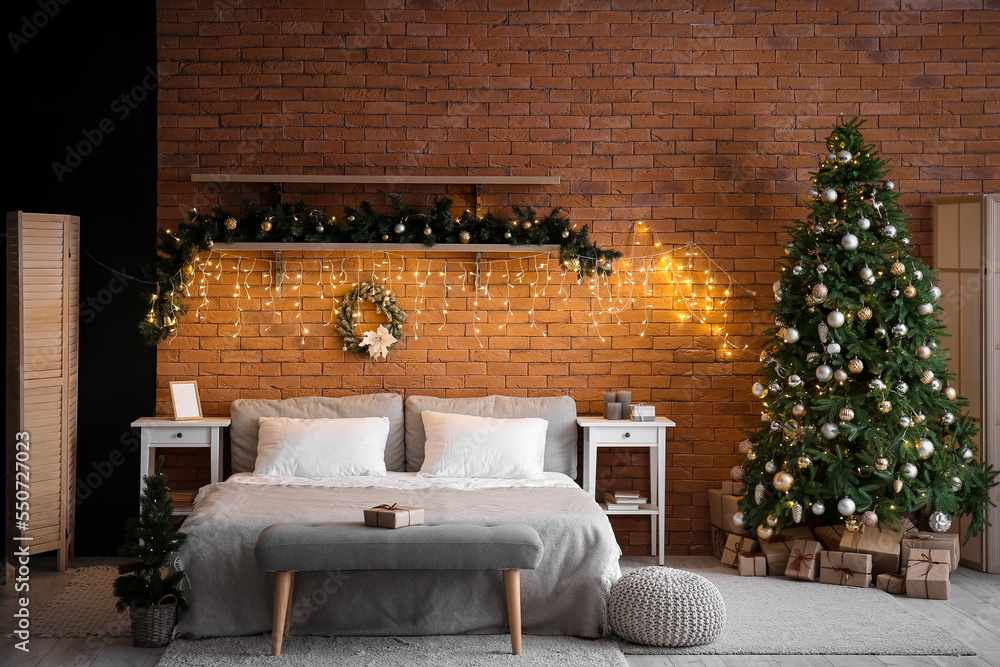 Interior of bedroom with Christmas trees, fir branches and glowing lights