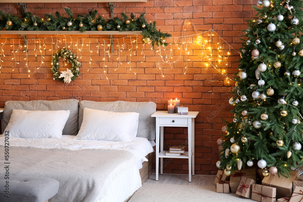 Interior of bedroom with Christmas tree, fir branches and glowing lights