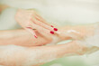 young woman hands and feet covered with foam inside white bath 