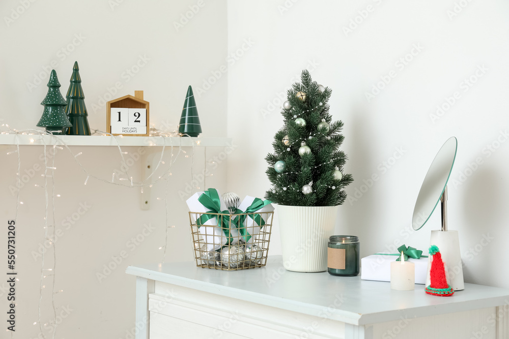 Small Christmas tree with presents, candles and mirror on shelf in light room