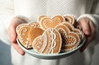 Woman holding plate with tasty heart shaped gingerbread cookies, closeup