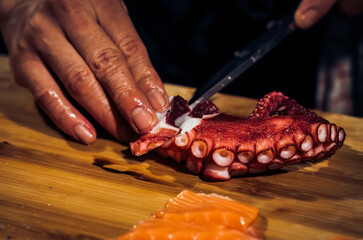 Wall Mural - Close up of Chef cook hands chopping octopus for traditional Asian cuisine with Japanese knife. Professional Sushi chef cutting seafood japanese chefs are making octopus sashimi. Dark Tone