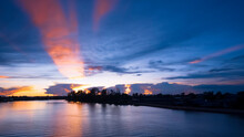 Dramatic Dusk Sky In The Evening With Majestic Orange Sunlight On Dark Blue Clouds Over Riverbank After Sundown