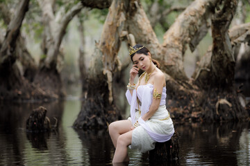 beautiful  Thai asian woman in white dress local tradition costume in the name is Nakee, sitting on tree stump in the lake in the botannical garden rayong thailand, 