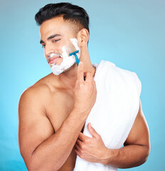 Poster - Man, shaving face and studio for wellness, skincare and towel with happiness by blue background. Model, facial hair removal and cosmetic foam for skin, self care and beauty with cosmetics by backdrop