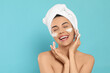 © New Africa - Happy young woman washing face with cosmetic product on light blue background, space for text