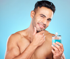 Poster - Beauty, cosmetics and man with cologne in studio on blue background for wellness, self care and luxury. Skincare, grooming and Indian male model with perfume, fragrance and scent in bottle