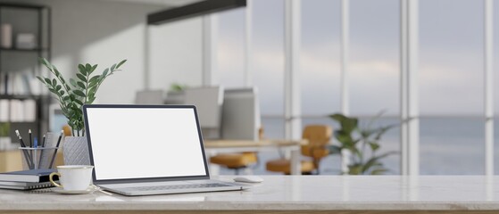 Modern office desk workspace with laptop mockup over blurred modern office in the background.