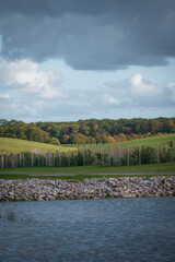 Wall Mural - Autumn colors on trees and rolling green hills and water as layers outside Lund Sweden