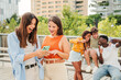 © Jose Calsina - Two attractive and cheerful smiling women looking and showing the last funny and entertaining news on their smartphone outside at the university campus. At background, three young friends, having fun