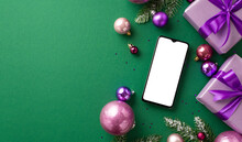 New Year Celebration Concept. Top View Photo Of Smartphone Lilac Gift Boxes With Bows Violet And Pink Baubles Fir Branches In Snow And Purple Sequins On Isolated Green Background With Empty Space
