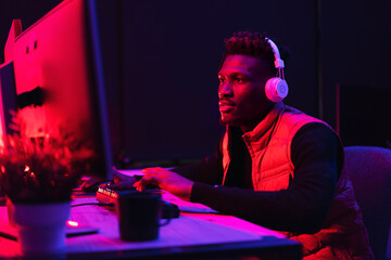 Young African man playing video game on computer. Streamer guy sitting at home and plays another match.