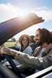 © CarlosBarquero - Vertical A young Caucasian couple driving in a convertible car. A cheerful boyfriend with his pretty bride travel in a vehicle enjoying the freedom of a weekend trip. Smiling people having fun