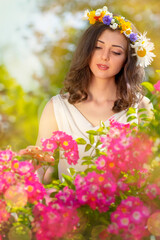 Fairy tale image art photo. Outdoor close up portrait of young beautiful happy smiling fantasy woman. Young goddess enjoys spring nature in bright sunlight and many pink roses