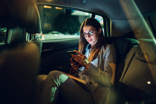 business woman using smartphone while sitting in a backseat of a car at night