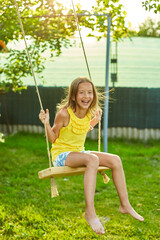 Wall Mural - Happy barefoot laughing child girl swinging on a swing in sunset summer day