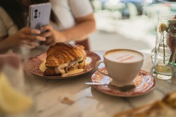 Sticker - Closeup of a table with a croissant sandwich and a cappuccino