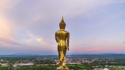 Wall Mural - Golden standing Buddha statue overlook city on mountain at Wat Phrathat Khao Noi temple; zoom out – time lapse