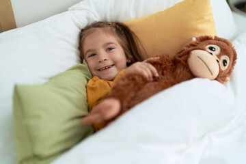 Poster - Adorable hispanic girl hugging monkey doll lying on bed at bedroom