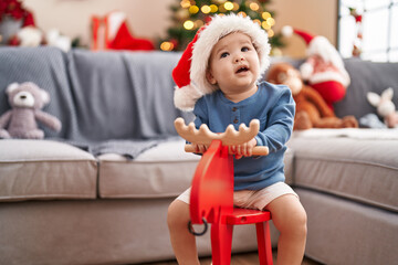 Sticker - Adorable caucasian baby playing with reindeer rocking by christmas tree at home