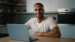 © Yuliia - Smiling African millennial man guy American male user freelancer at home kitchen finish distant work with laptop satisfied with computer app online website networking shopping looking at camera smile