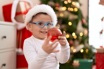 Adorable hispanic toddler smiling confident holding christmas decoration ball at home