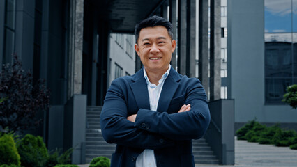 Male portrait in city outdoors 40s middle-aged smiling positive adult Asian Korean man entrepreneur manager company CEO realtor businessman boss leader confident employer posing crossing hands smile