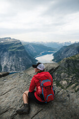 a young tourist woman in red jacket sitting on the rock enjoying the beautiful view on norwegian ver