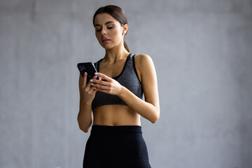 Attractive healthy young woman with a fitness mat using mobile phone at the studio