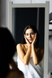 © F8  \ Suport Ukraine - Self-Care Concept. Portrait of attractive young female looking at mirror. Beautiful Woman Wearing White Silk Robe Touching Soft Skin On Face And Smiling, Enjoying Her Reflection, Selective Focus