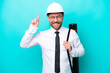 © luismolinero - Middle age architect man with helmet and holding blueprints isolated on blue background pointing up a great idea