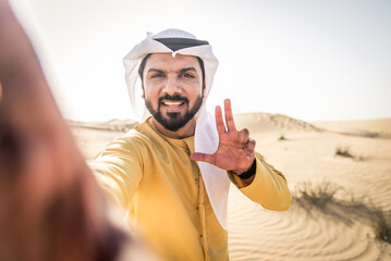 Wall Mural - Portrait of handsome middle-eastern man wearing traditional emirates kandora in the desert of Dubai, UAE