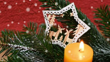 Wall Mural - Burning orange candle lit with Christmas decoration, green fir twig and effect of falling snow. Christmas Atmosphere