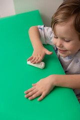 Wall Mural - Smiling boy makes Christmas crafts on a green table from white polymer clay