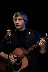 Male musician with guitar in hands playing and posing on black background in blue scenic light