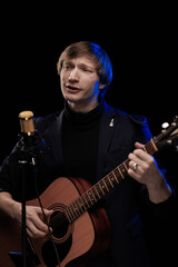 Male musician with guitar in hands playing and posing on black background in blue scenic light