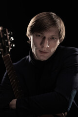 Male musician with guitar in hands playing and posing on black background in blue scenic light