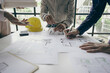 © ArLawKa - Engineering team meeting for colleagues discussing and reviewing blueprints at desk in office Engineers and workers planning for construction and renovation building projects in workplace