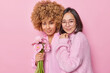 © wayhome.studio  - Horizontal shot of mixed race young women stand closely to each other hold bouquet of gerbera flowers smile gently enjoy spending time together isolated over pink background. Friendship concept
