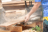 Fototapeta  - Joiner, Man's hand scouring a wooden board on a thickness machine in garden. Carpenter working with electric planer on wooden beam, plank.DIY concept