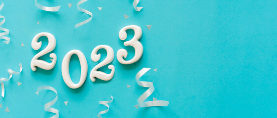 Wall Mural - close up number 2023 shape wood on blue color background with rolling ribbon and confetti for happy 