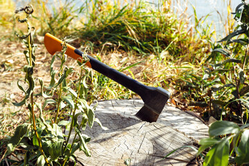 Universal orange red black modern axe with Shock absorbing fibreglass handle on dry stump log on lake coast in grass. Hiking and picnic.